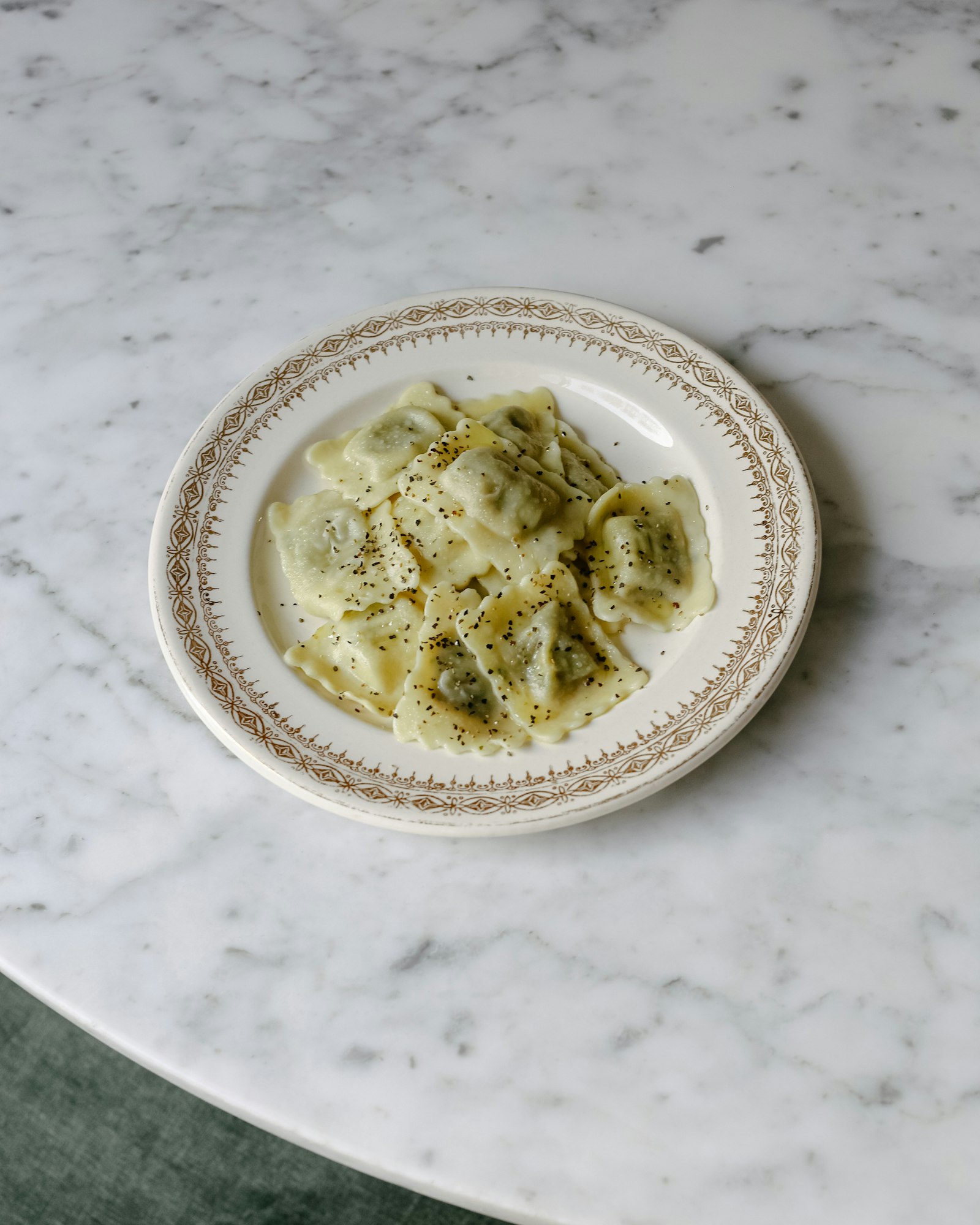 Ravioli ricotta e spinaci conditi con burro e pepe nero in un piatto su tavolo di marmo
